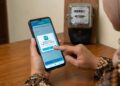 Ilustrasi seorang pelanggan sedang menggunakan aplikasi PLN Mobile di ponsel pintarnya untuk mengklaim promo diskon tambah daya listrik.